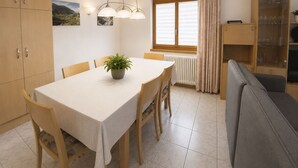 A dining area with a table, chairs, a potted plant, a window with curtains, and a built-in cabinet with glassware. - Residenz Darianne Leukerbad # 5-bed apartment, Dusche und Bad, WC by Interhome (Leukerbad)