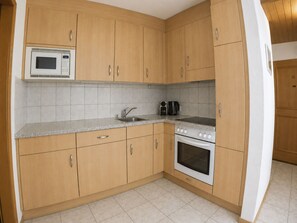 A kitchen with wooden cabinets, a microwave, a sink, a coffee maker, and an oven. - Residenz Darianne Leukerbad # 5-bed apartment, Dusche und Bad, WC by Interhome (Leukerbad)