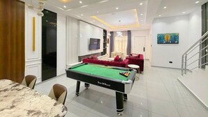 Een moderne woonkamer met een pooltafel, een eethoek en een trap.