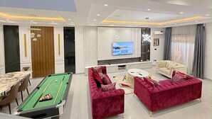 Een moderne woonkamer met een pooltafel, rode banken, een televisie en een eethoek.