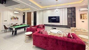 Een moderne woonkamer met een pooltafel, een rode bank en een flatscreen televisie.