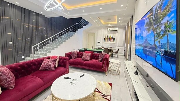 Een moderne woonkamer met een rode bank, een witte salontafel, een grote flatscreen televisie en een trap naar een hoger gelegen verdieping.