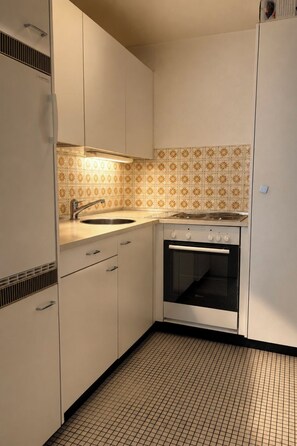Eine Küche mit weißen Schränken, einer gefliesten Spritzschutzwand, einer Edelstahl-Spüle und einem eingebauten Backofen.