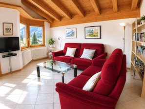 Ein Wohnzimmer mit einem roten Sofa, einem Glastisch, einem Fernseher und einem Bücherregal.