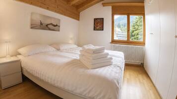 A bedroom with a bed, a nightstand, a radiator, and a window with a view of trees.