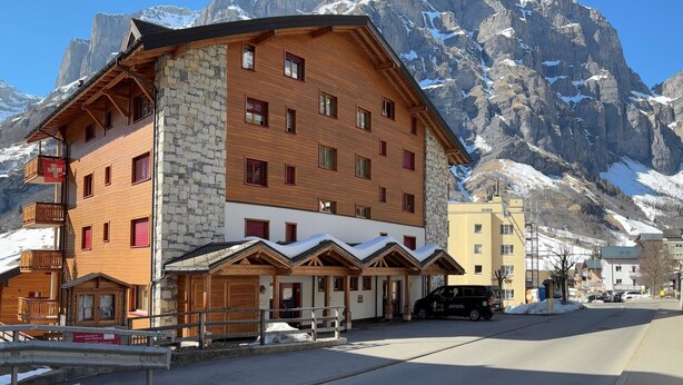 A multi-story hotel with a stone facade, wooden balconies, and a mountain backdrop. - Residenz Darianne Leukerbad # 4-bed apartment, Dusche, WC by Interhome (Leukerbad)