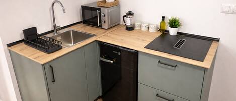 A compact kitchen with a sink, microwave, coffee maker, and a small potted plant.
