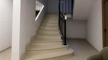 Un escalier avec une rampe noire, des marches recouvertes d’une moquette beige et un plancher de couleur claire.