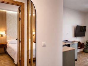 Ein modernes Hotelzimmer mit Bett, Nachttisch, Lampe und einem an der Wand montierten Fernseher.