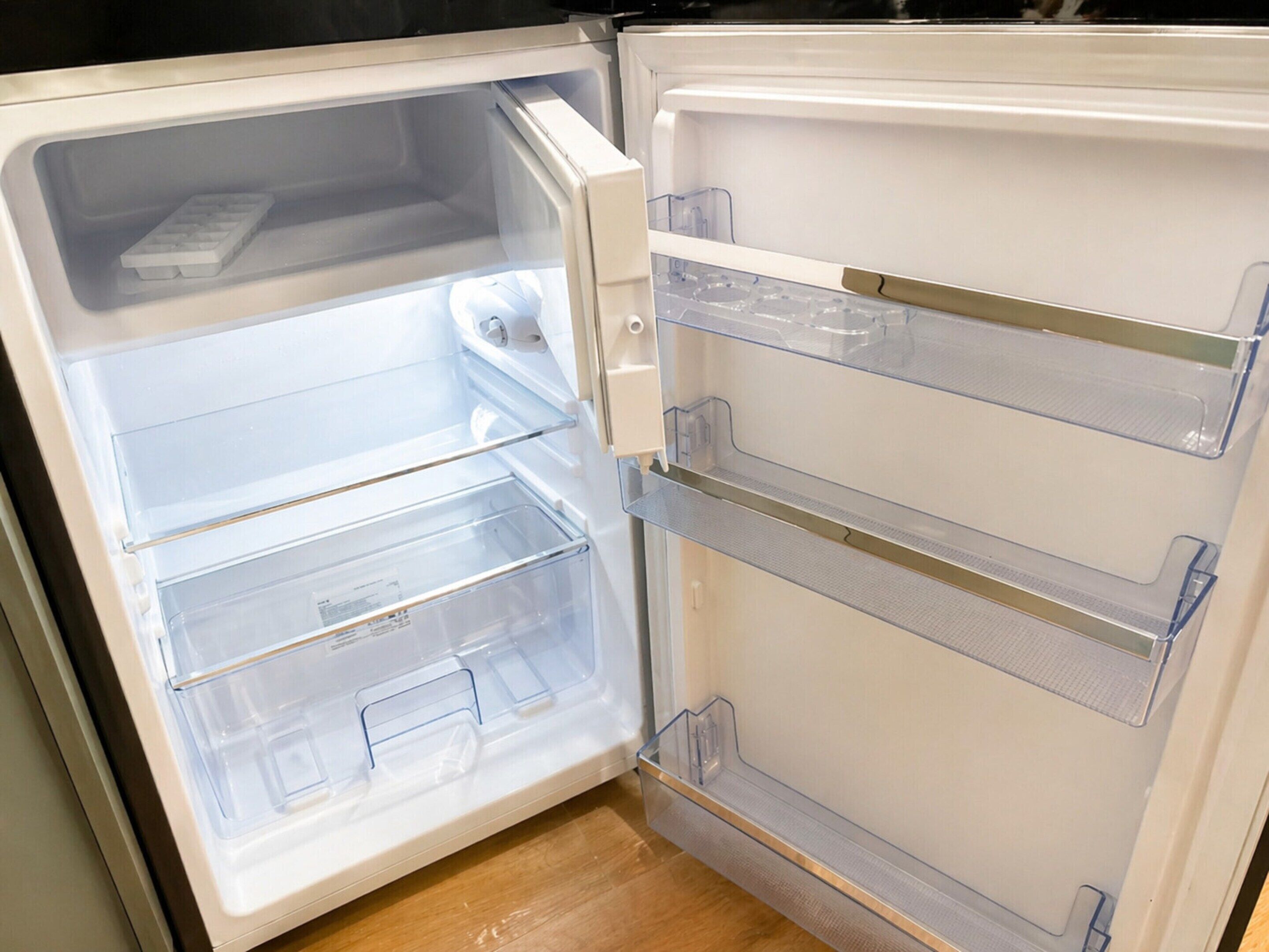 Ein offener Kühlschrank mit klaren Plastikregalen und einem Gefrierfach.