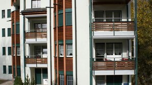 Ein mehrstöckiges Wohngebäude mit Balkonen, einer Terrasse mit Sitzgelegenheiten und einem kleinen Garten.