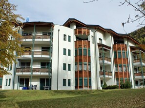 A multi-story building with balconies, a flat roof, and a grassy area in front. - La Promenade 11 # 6-bed apartment, Bad, WC 6-Bettwohnung, Bad, WC by Interhome (Leukerbad)