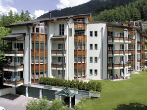 A multi-story residential building with balconies, a green lawn, and a mountainous backdrop. - La Promenade 11 # 6-bed apartment, Bad, WC 6-Bettwohnung, Bad, WC by Interhome (Leukerbad)