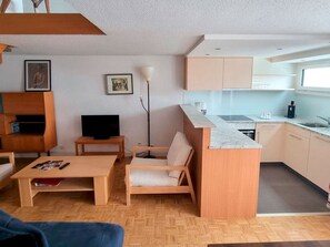 Ein gemütlicher Wohnbereich mit Sofa, Couchtisch, Fernseher, Stehlampe und Küchenzeile.