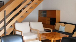 Moderni olohuone, jossa on puinen portaikko, sohvaryhmä, sohvapöytä ja senkki.