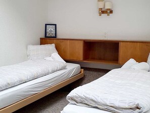 A room with two single beds, a wooden headboard, a small shelf, and a wall-mounted light fixture. - Fortuna 307 # 5-bed apartment, Dusche, WC 5-Bettwohnung, Dusche, WC by Interhome (Leukerbad)