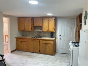 A kitchen with wooden cabinets, a sink, a stove, and a door.