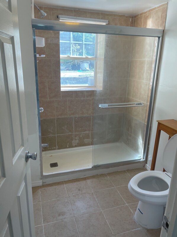 A bathroom with a glass-enclosed shower, a toilet, and a window providing natural light.