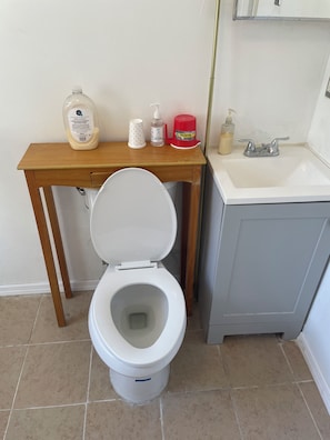 A bathroom with a toilet, a sink, and a small table with toiletries.