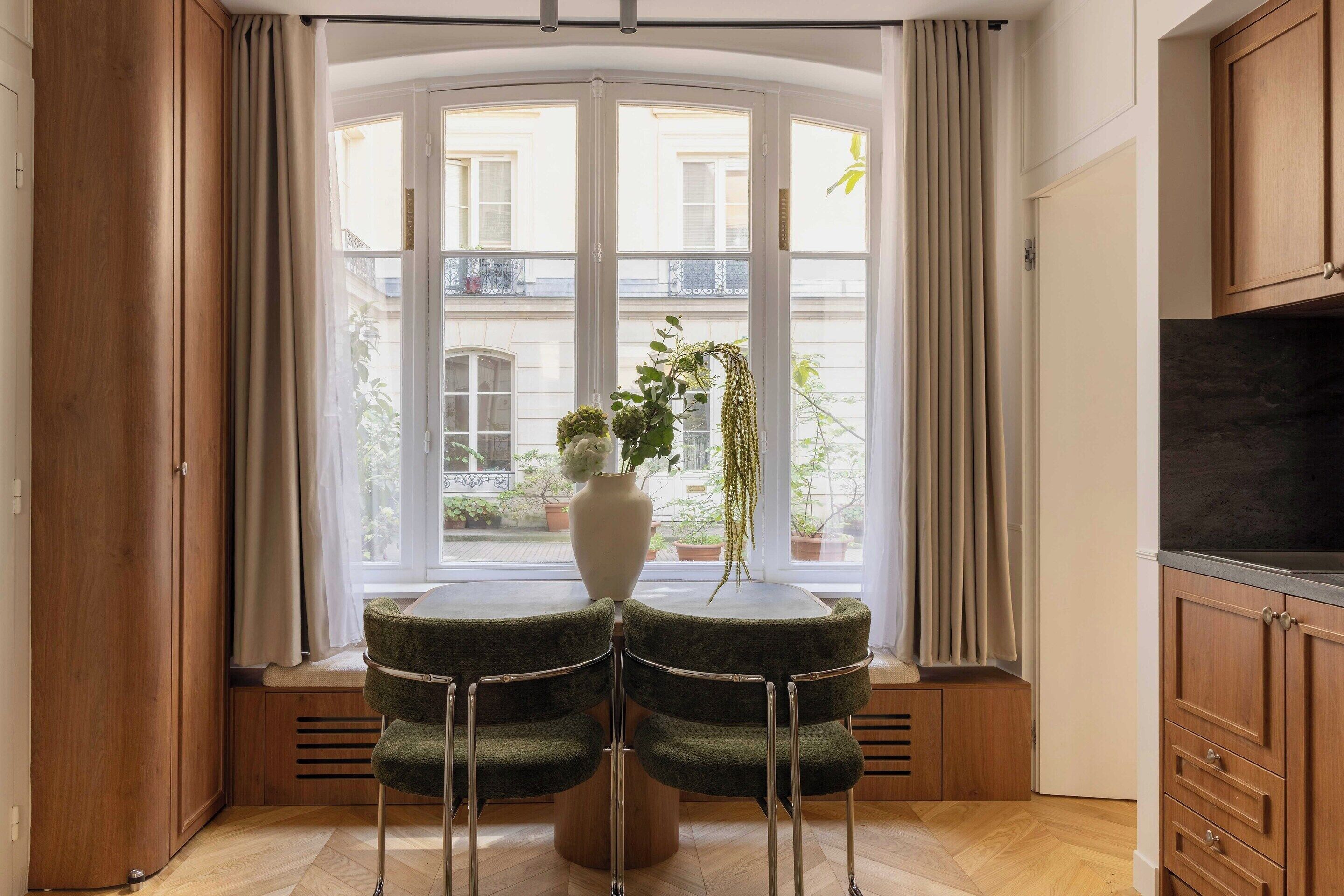 Ein Zimmer mit einem gebogenen Fenster, einem runden Tisch mit vier Stühlen, einer Pflanzvase und Holzschränken.