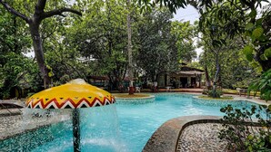 A swimming pool with a colorful water feature, surrounded by lush greenery and a building in the background.