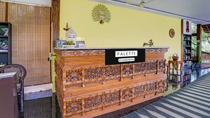 A reception desk with a sign reading 'PALETTE,' a decorative wall with a sun-like design, a ceiling fan, and a striped floor.