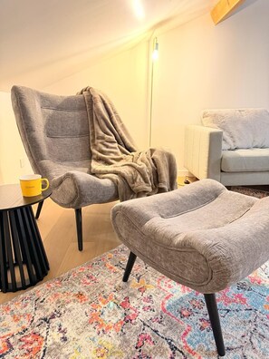A living room with a grey armchair, a small round table with a yellow mug, a grey ottoman, and a colorful rug. - The Ax Bubble (Ax-les-Thermes)