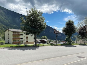 A building with balconies, a parking lot, and a mountain backdrop. - Majesta Leukerbad # 6-bed apartment, Dusche und Bad, WC by Interhome (Leukerbad)