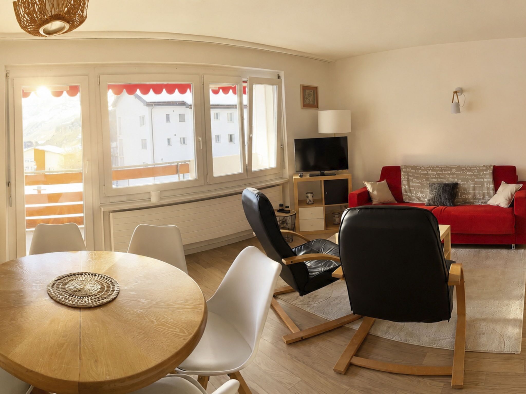 A living room with a red sofa, black chairs, a wooden table, and a TV on a wooden stand.