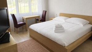 Een hotelkamer met een bed, een bureau, een stoel, een televisie en een raam met gordijnen.