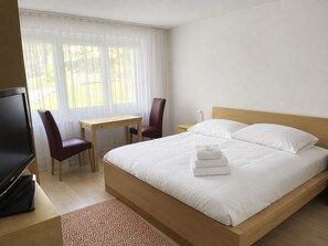 A hotel room with a bed, a desk, a chair, a TV, and a window with curtains. - Majesta Leukerbad # 6-bed apartment, Dusche und Bad, WC by Interhome (Leukerbad)