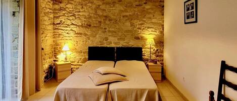 Ein Schlafzimmer mit Stehwand, einem Bett mit zwei Kissen, zwei Nachttischen mit Lampen und einem Holzstuhl.