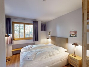Ein Schlafzimmer mit zwei Betten, einem Fenster mit Vorhängen, einem Nachttisch mit Lampe und einem Wandbild.