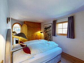 Una habitación de hotel con cama, lámpara, ventana con cortinas y un armario de madera.