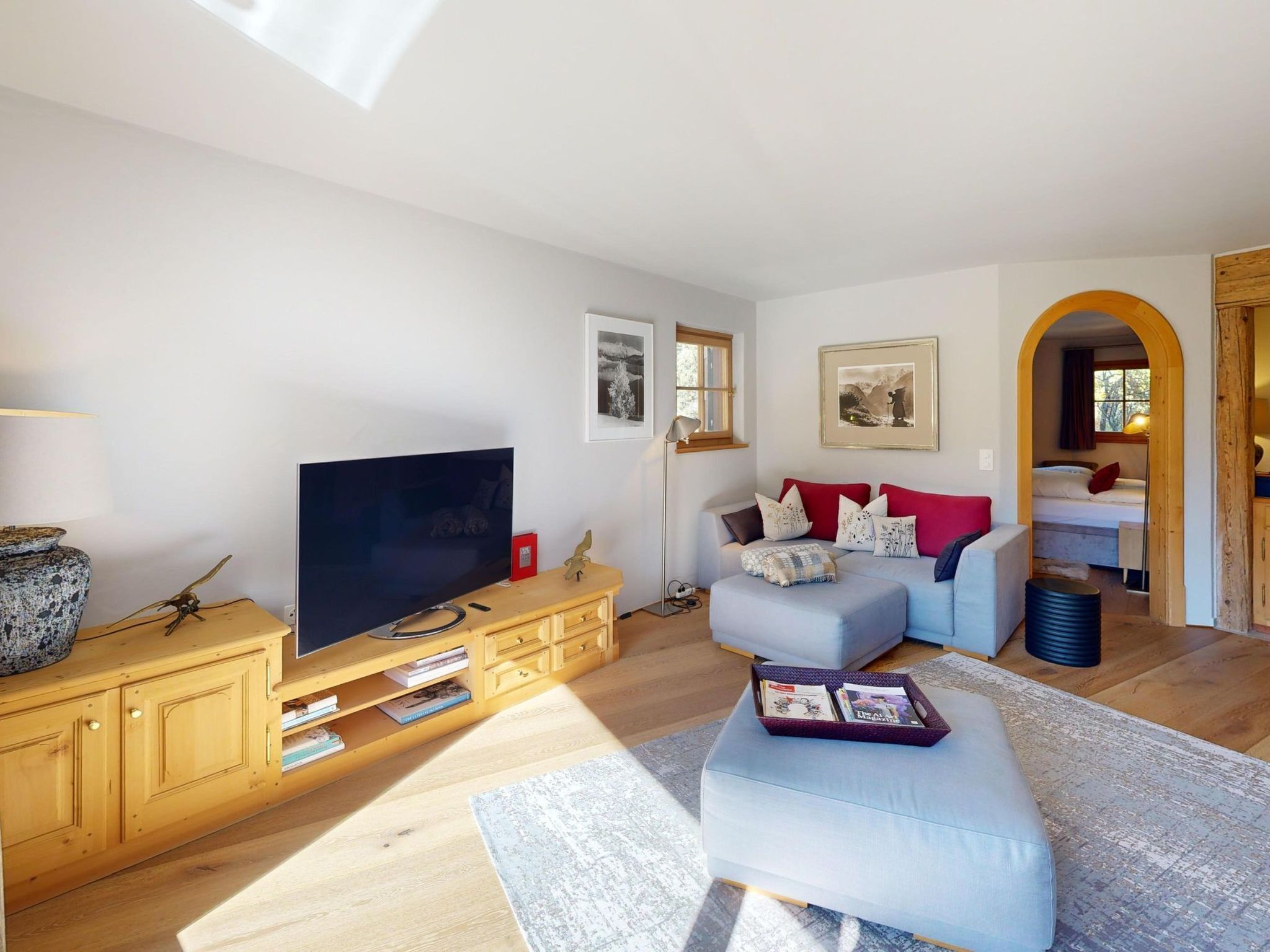 Een moderne woonkamer met een flatscreen televisie, een houten tv-meubel, een lichtblauwe bank en een rode kussen.