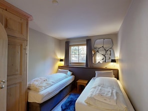 A hotel room with two beds, a window, a wall-mounted mirror, and a wooden door. - Apartment Üerts by Interhome (St. Moritz)