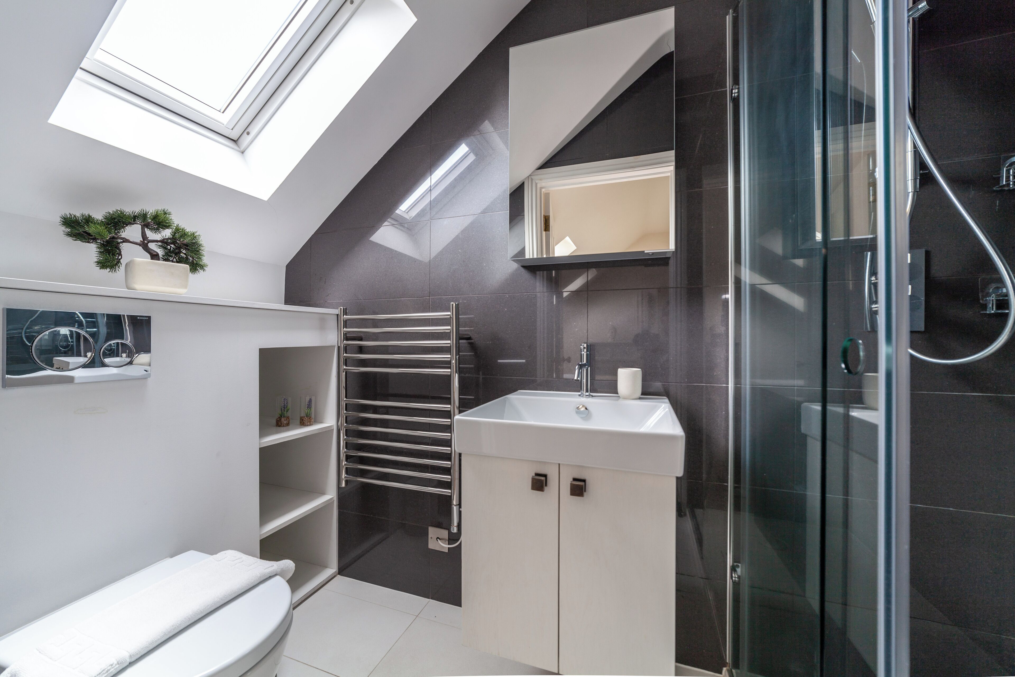 A modern bathroom with a skylight, a glass shower enclosure, a white sink, and a towel rack.