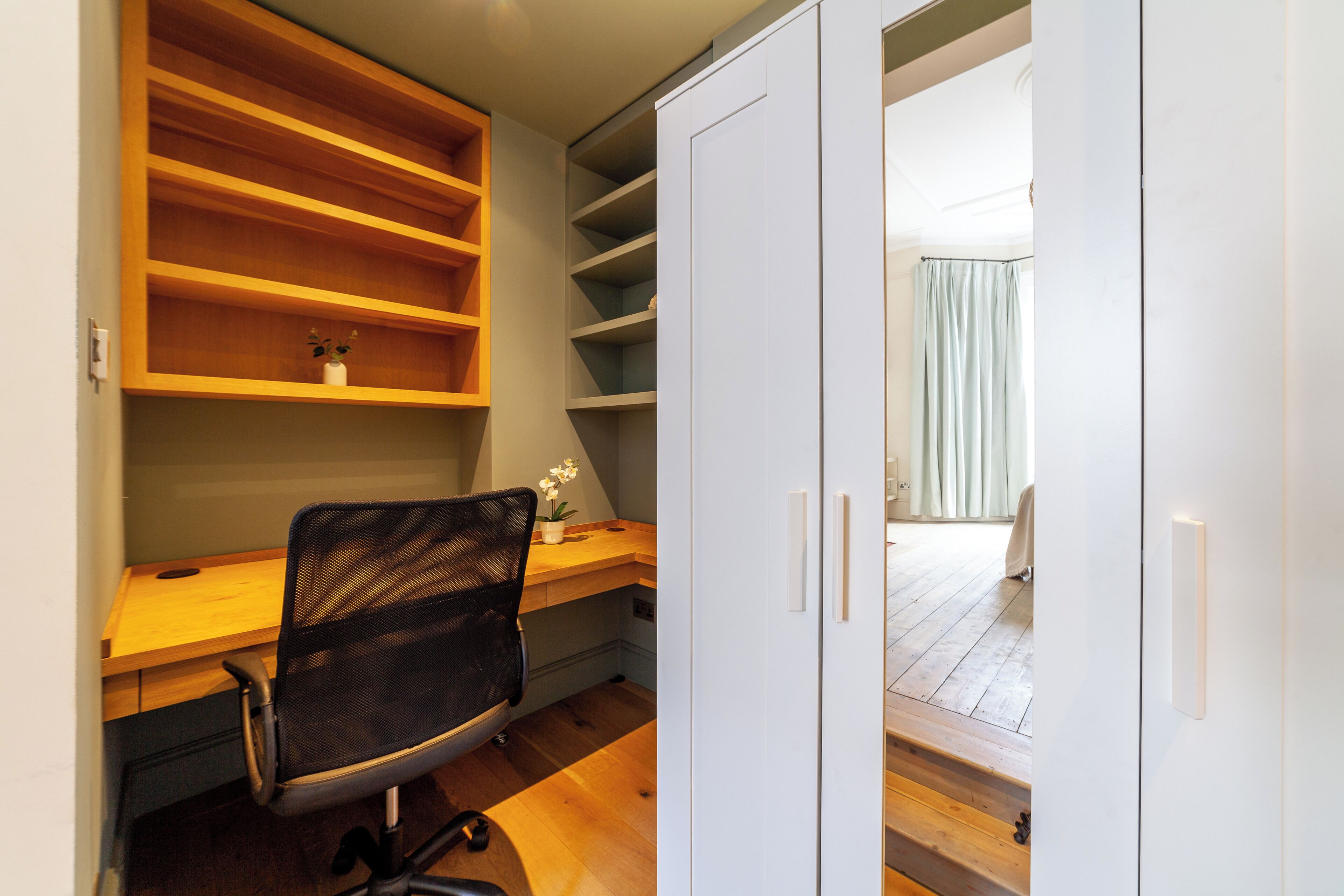 A room with a wooden desk, a black office chair, and a white wardrobe.