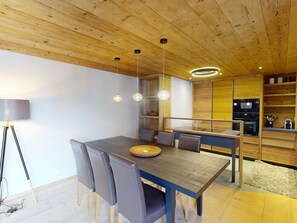A modern dining area with a wooden table and chairs, a built-in kitchen, and a ceiling with exposed beams. - Apartment Skyline 406 by Interhome (St. Moritz)