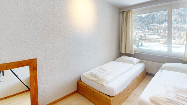 A bedroom with a bed, a wooden bench, and a window with a view of a snowy landscape. - Apartment Skyline 406 by Interhome (St. Moritz)