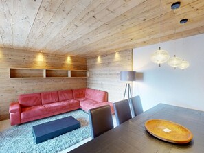 A modern interior with a wooden ceiling, a red leather sofa, a dining table with chairs, and pendant lighting. - Apartment Skyline 406 by Interhome (St. Moritz)