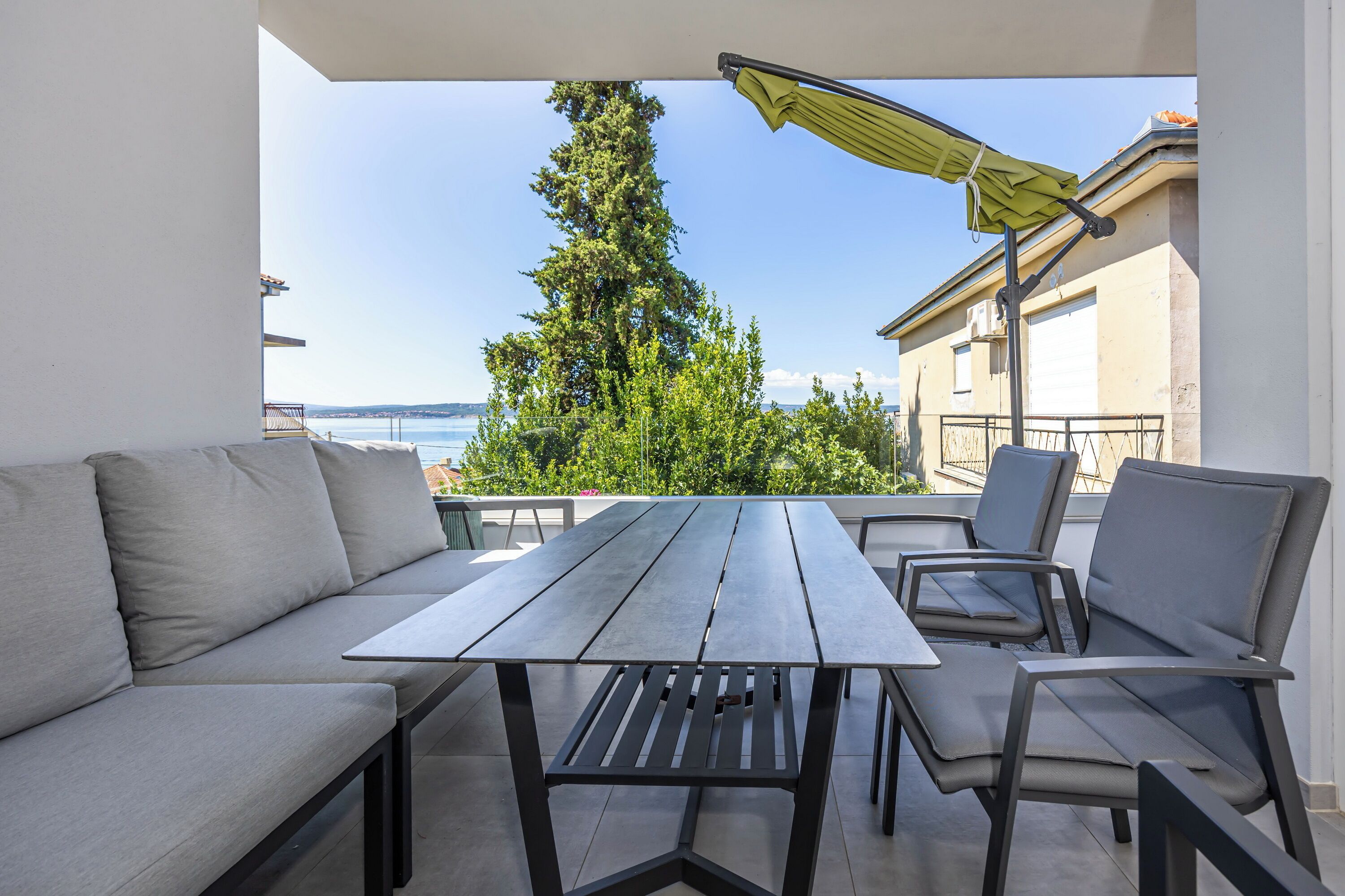 An outdoor seating area with a table and chairs, overlooking a body of water and a tree.
