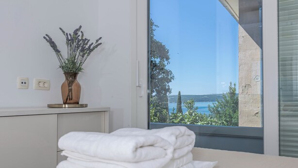 Une salle de bain avec une fenêtre donnant sur un paysage côtier, une pile de serviettes blanches et une plante en pot.