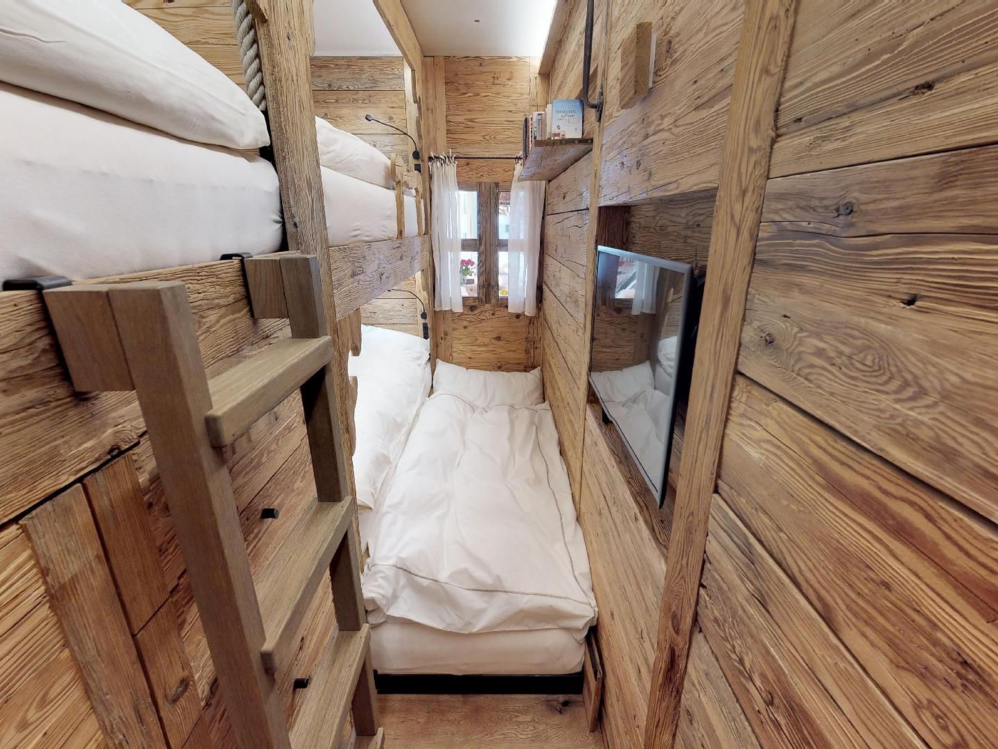A narrow wooden room with bunk beds and a small window.