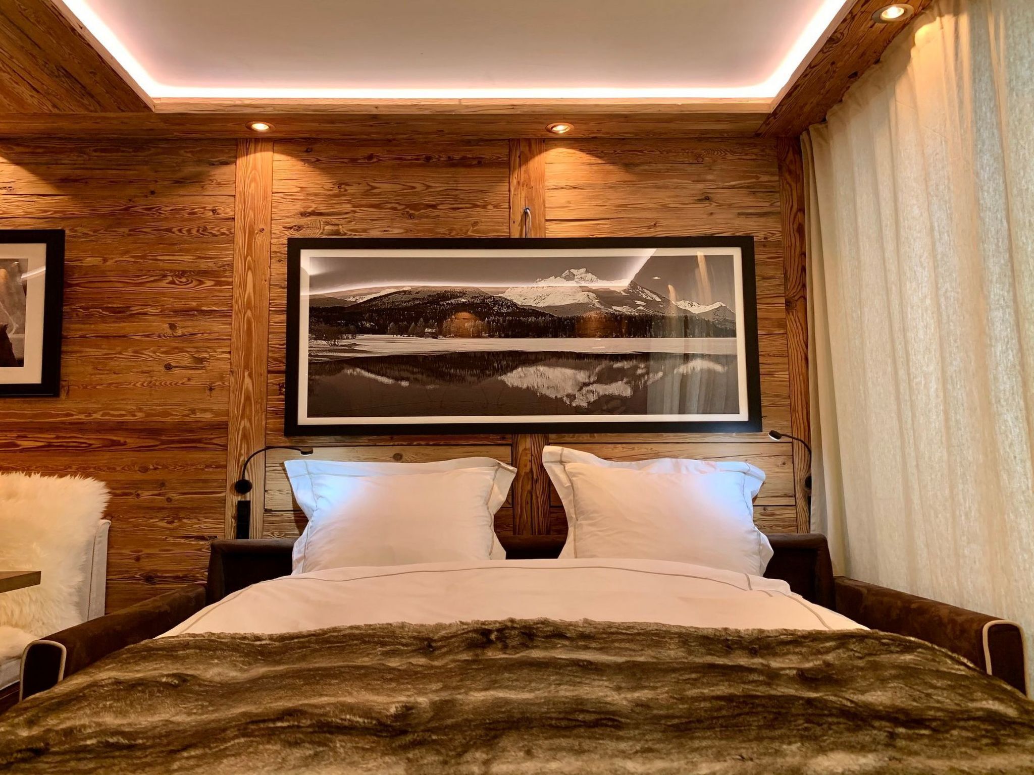 A bedroom with a large bed, wooden walls, a framed picture on the wall, and a window with curtains.