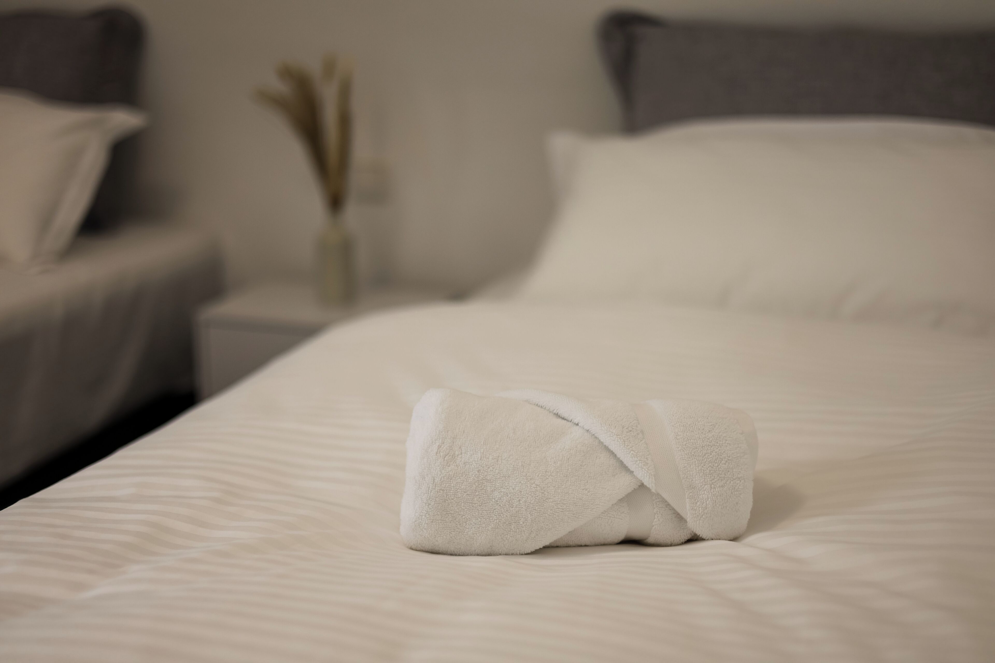 A neatly made bed with a folded white towel, a bedside table with a vase, and a pillow on the bed.