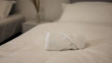 A neatly made bed with a folded white towel, a bedside table with a vase, and a pillow on the bed.