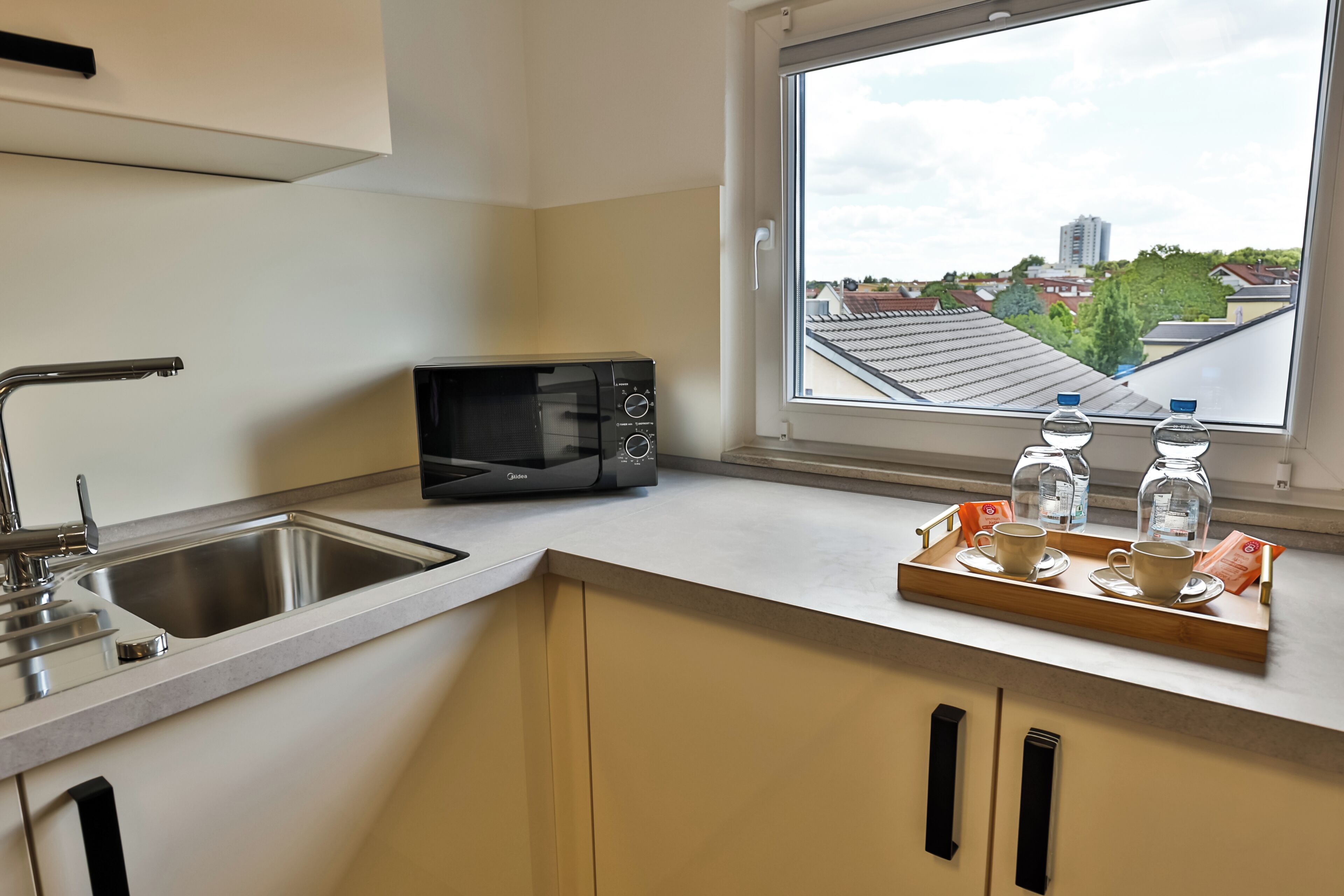 A kitchen with a microwave, sink, and window with a view of buildings.