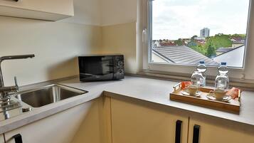 A kitchen with a microwave, sink, and window with a view of buildings.