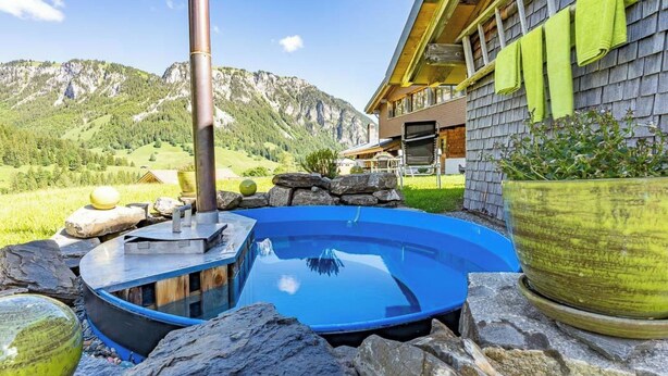 Un jacuzzi en zona montañosa, con una casa de madera y vistas a la montaña.